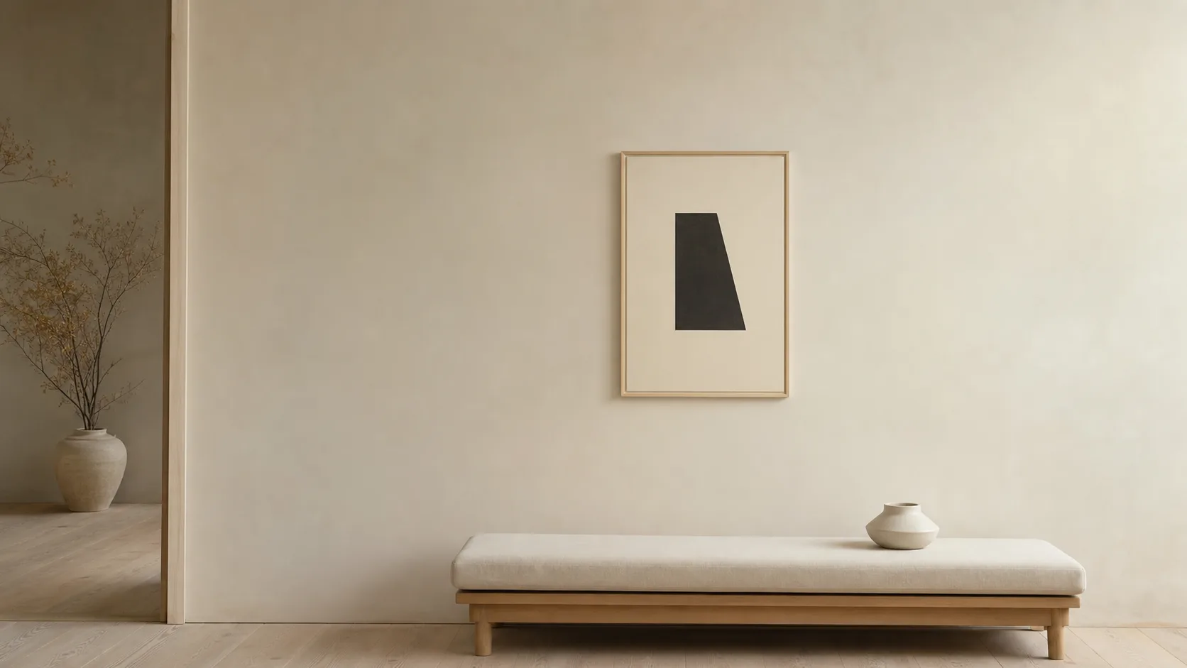 Liten minimalistisk tavla med en mörk geometrisk form på krämvit yta och mycket tom vägg runtom